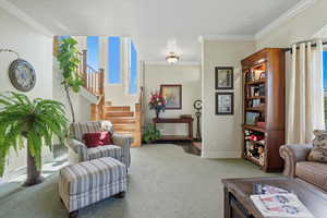 Living area featuring ornamental molding, healthy amount of natural light, light carpet, and stairs