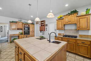 Kitchen with a center island with sink, brown cabinetry, light tile patterned flooring, tile countertops, and recessed lighting