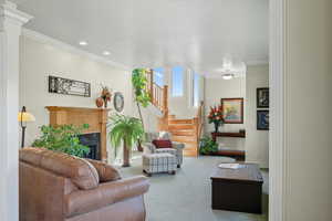 Carpeted living room with crown molding, a fireplace, stairs, and recessed lighting