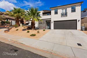 View of front of house with stucco siding, a garage, driveway, stone siding, and a tile roof