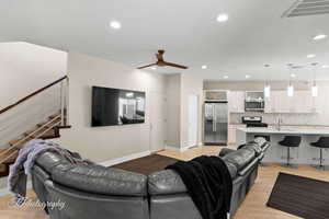 Living area with light wood-type flooring, a ceiling fan, recessed lighting, and stairs
