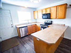 Kitchen featuring appliances with stainless steel finishes, a peninsula, light countertops, and dark wood finished floors