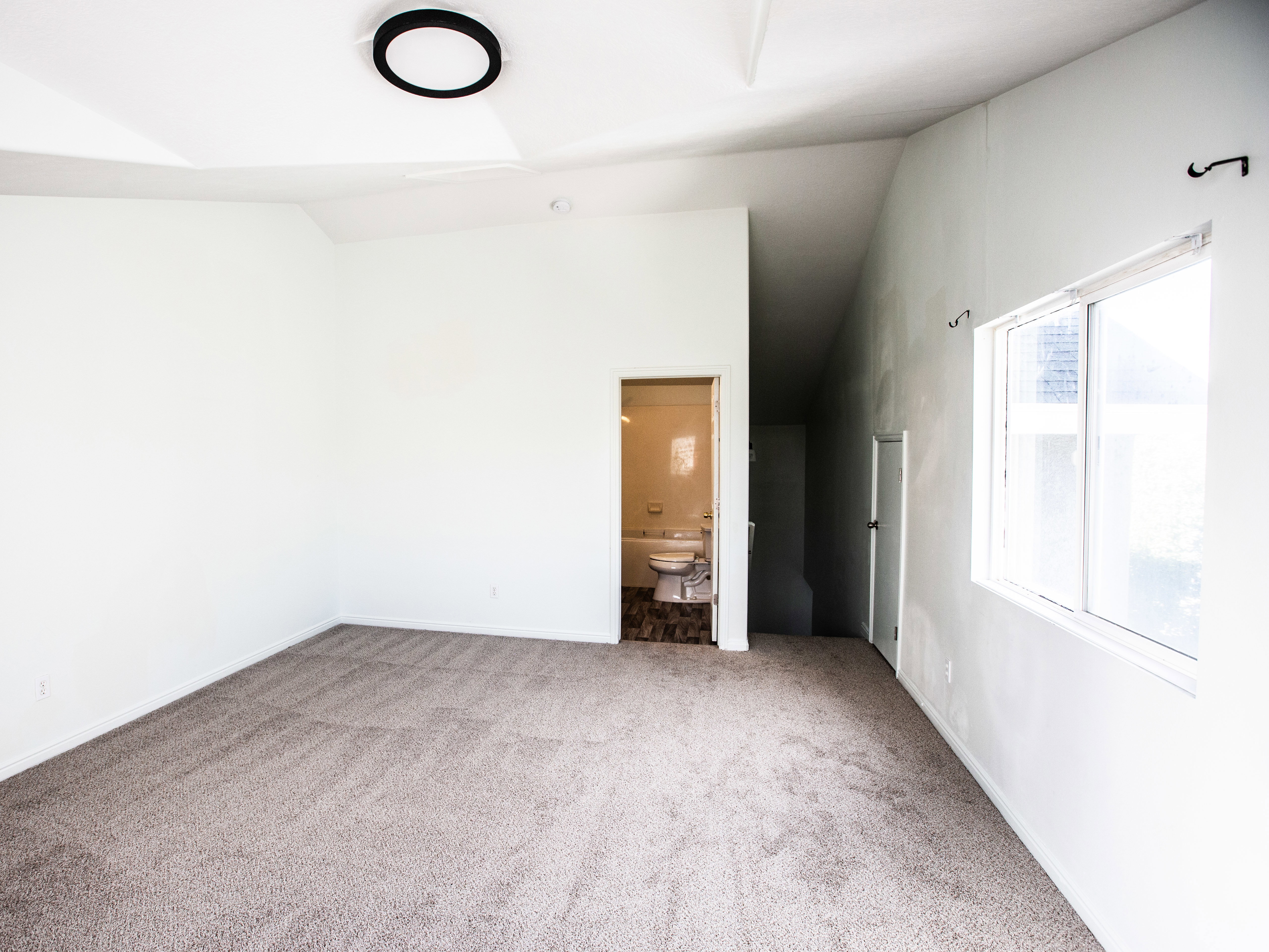 Unfurnished bedroom with vaulted ceiling, ensuite bathroom, and light colored carpet
