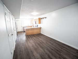 Kitchen with light countertops, a peninsula, dark wood finished floors, appliances with stainless steel finishes, and open floor plan