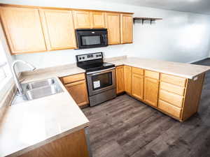 Kitchen with a peninsula, electric range, light countertops, black microwave, and dark wood finished floors