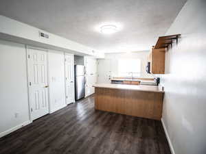 Kitchen with a peninsula, light countertops, a textured ceiling, stainless steel appliances, and dark wood-type flooring