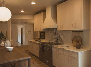 Kitchen featuring range with two ovens, wall chimney range hood, tasteful backsplash, light stone countertops, and dark wood-type flooring