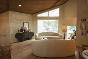Living area featuring wooden ceiling, wood finished floors, brick wall, and high vaulted ceiling