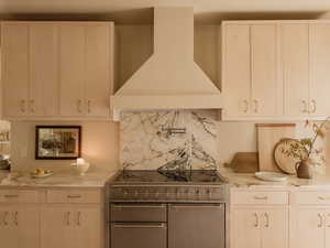 Kitchen featuring wall chimney exhaust hood, range with two ovens, light stone counters, and backsplash