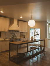 Kitchen featuring decorative backsplash, wall chimney range hood, dark wood-style flooring, pendant lighting, and recessed lighting