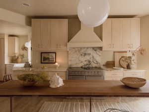 Kitchen with range with two ovens, decorative backsplash, light stone counters, and wall chimney range hood