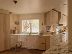 Kitchen with range with electric cooktop, wall chimney exhaust hood, light stone counters, light brown cabinets, and dark wood-type flooring