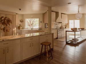 Kitchen with wall chimney exhaust hood, decorative backsplash, pendant lighting, dark wood-style floors, and light stone counters