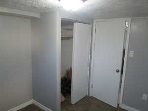 Unfurnished bedroom featuring a textured ceiling, dark carpet, and a closet