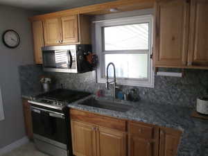 Kitchen with stainless steel appliances, decorative backsplash, and dark stone counters