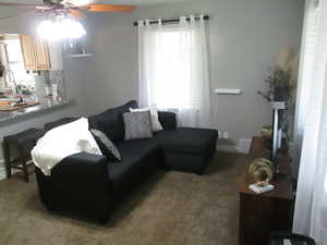 Carpeted living area featuring ceiling fan and baseboards