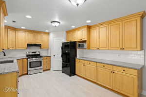 Kitchen with light stone counters, decorative backsplash, appliances with stainless steel finishes, light brown cabinets, and recessed lighting