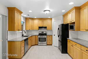 Kitchen featuring light stone counters, appliances with stainless steel finishes, tasteful backsplash, and recessed lighting