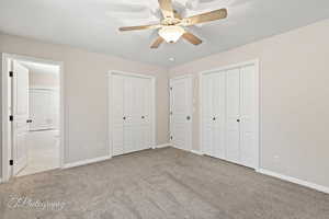 Unfurnished bedroom with two closets, light colored carpet, ensuite bathroom, and ceiling fan