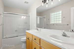 Full bathroom featuring bath / shower combo with glass door and double vanity