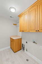 Laundry area with cabinet space, light wood-style flooring, electric dryer hookup, hookup for a gas dryer, and a textured ceiling