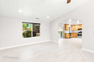 Unfurnished living room featuring arched walkways, recessed lighting, ceiling fan, and light wood-style floors