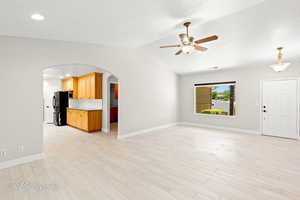 Unfurnished living room featuring light wood finished floors, arched walkways, a ceiling fan, vaulted ceiling, and recessed lighting