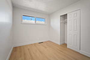 Unfurnished bedroom featuring a textured ceiling, light wood-type flooring, and a closet