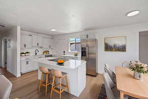 Kitchen with stainless steel fridge, a breakfast bar area, light wood-type flooring, white cabinets, and a center island