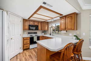 Kitchen featuring brown cabinetry, light countertops, white refrigerator with ice dispenser, and range with electric cooktop