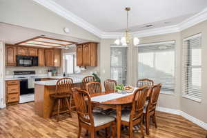 Dining area with light wood finished floors, a chandelier, and crown molding