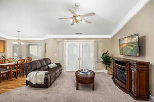 Living room with french doors, ornamental molding, carpet floors, ceiling fan, and a glass covered fireplace