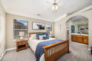 Bedroom with light carpet, crown molding, ceiling fan, arched walkways, and ensuite bath