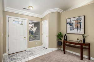Foyer entrance with light tile patterned floors, ornamental molding, light carpet, and vaulted ceiling