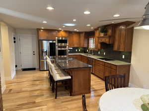 Kitchen featuring dark stone counters, brown cabinetry, appliances with stainless steel finishes, recessed lighting, and tasteful backsplash