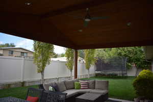 Fenced backyard featuring an outdoor hangout area, a trampoline, a patio area, and a ceiling fan