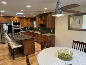 Kitchen featuring dark stone countertops, stainless steel appliances, decorative backsplash, brown cabinetry, and recessed lighting