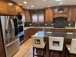 Kitchen with stainless steel appliances, dark stone counters, brown cabinets, and recessed lighting