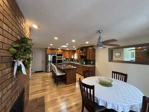 Dining area featuring brick wall, recessed lighting, light wood finished floors, a ceiling fan, and a fireplace