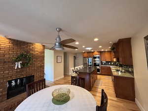 Kitchen with a fireplace, dark stone countertops, recessed lighting, a ceiling fan, and light wood-style floors