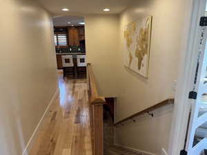 Hallway featuring light wood finished floors, an upstairs landing, arched walkways, and recessed lighting