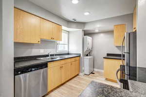 Kitchen featuring light brown cabinetry, appliances with stainless steel finishes, dark countertops, light wood-style floors, and recessed lighting