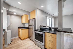 Kitchen featuring appliances with stainless steel finishes, a peninsula, light brown cabinets, light wood-style floors, and washer / dryer