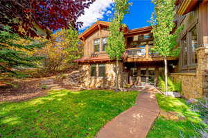 Back of property with a lawn, stone siding, french doors, and a balcony