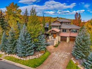 View of front facade with stone siding, a garage, concrete driveway, roof with shingles, and a balcony