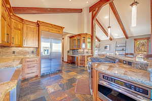 Kitchen featuring glass insert cabinets, appliances with stainless steel finishes, beam ceiling, light stone countertops, and decorative backsplash