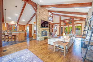 Living room with high vaulted ceiling, beamed ceiling, dark wood finished floors, a stone fireplace, and recessed lighting