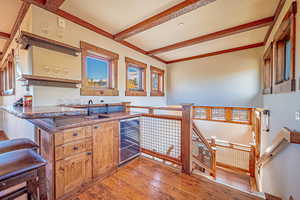Kitchen with light wood-style floors, open shelves, beverage cooler, brown cabinetry, and beamed ceiling