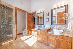 Bathroom featuring a stall shower, double vanity, decorative backsplash, and light wood-type flooring
