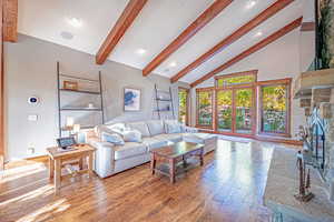 Living area featuring light wood finished floors, beamed ceiling, french doors, a fireplace, and high vaulted ceiling